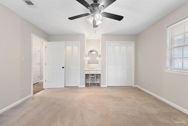 unfurnished bedroom featuring a textured ceiling, ceiling fan, light carpet, and two closets