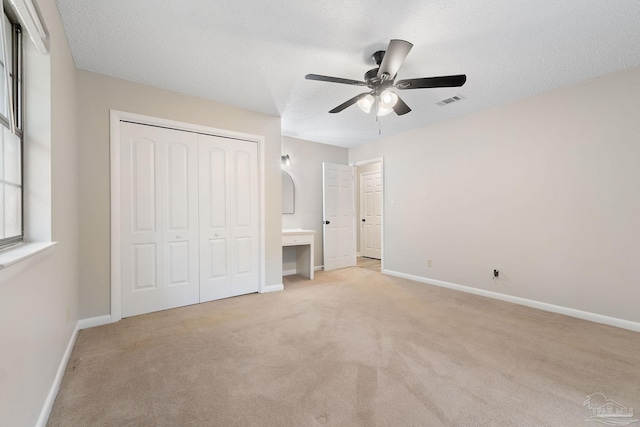 unfurnished bedroom with ceiling fan, light carpet, and a textured ceiling