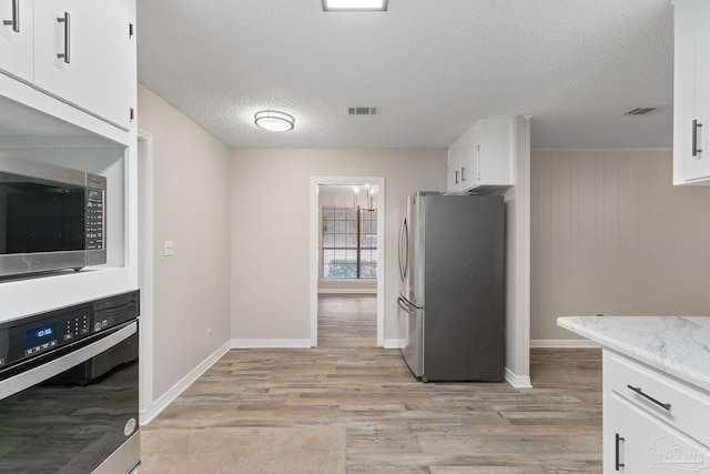 kitchen featuring white cabinets, light wood-type flooring, a textured ceiling, and appliances with stainless steel finishes