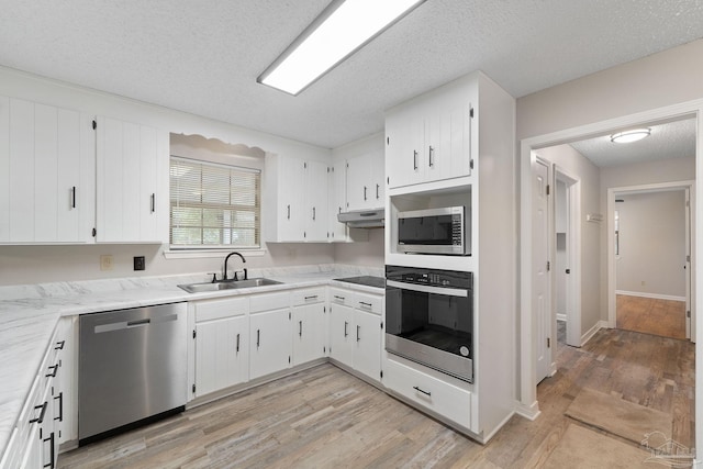 kitchen with sink, stainless steel appliances, a textured ceiling, white cabinets, and light wood-type flooring