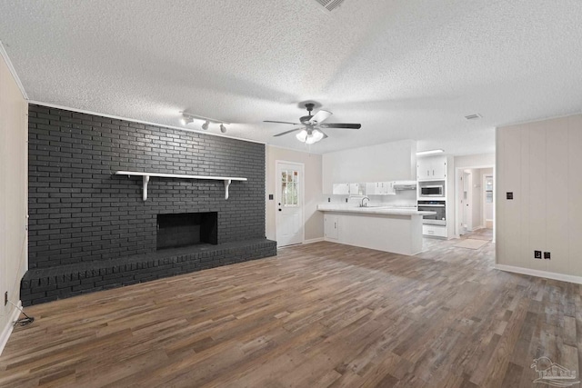 unfurnished living room featuring a brick fireplace, a textured ceiling, ceiling fan, sink, and wood-type flooring