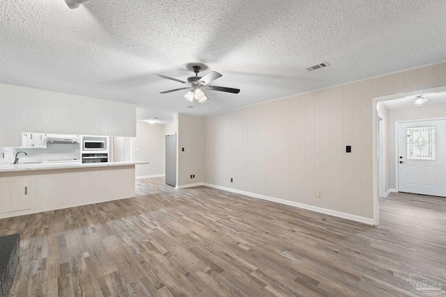 unfurnished living room with sink, wooden walls, ceiling fan, light wood-type flooring, and a textured ceiling