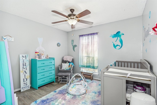 bedroom with ceiling fan, a nursery area, and light wood-type flooring