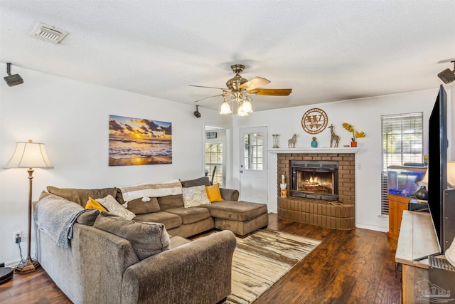 living room with a textured ceiling, ceiling fan, dark wood-type flooring, and a brick fireplace