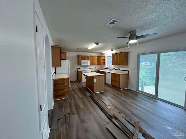 kitchen with white appliances, a textured ceiling, a kitchen island, ceiling fan, and dark wood-type flooring