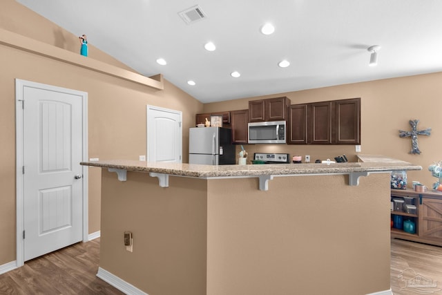 kitchen with visible vents, vaulted ceiling, light wood-style floors, appliances with stainless steel finishes, and a kitchen bar