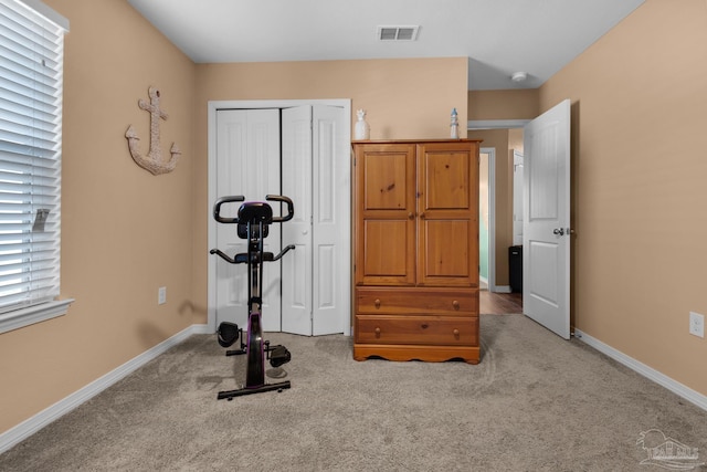 exercise room featuring visible vents, baseboards, and light colored carpet