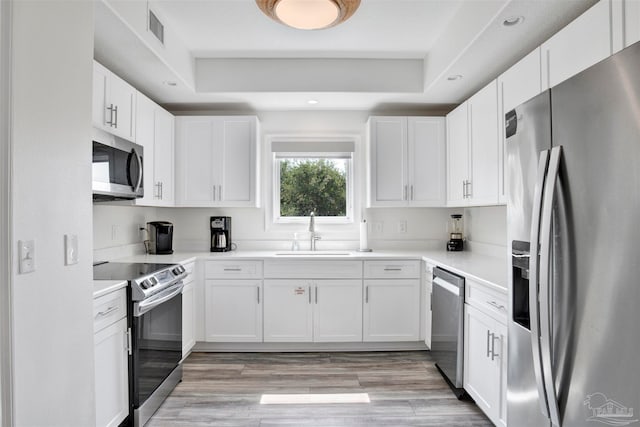 kitchen featuring sink, stainless steel appliances, a raised ceiling, white cabinets, and light wood-type flooring