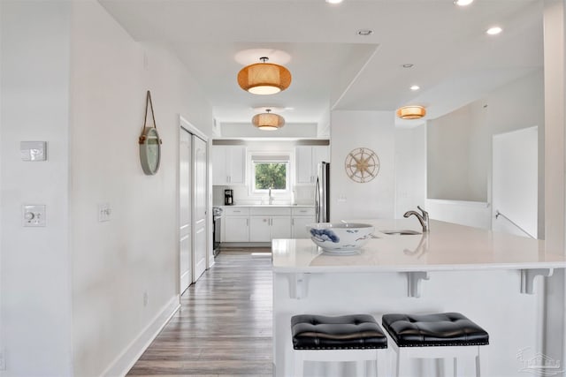 kitchen with a kitchen breakfast bar, stainless steel appliances, sink, white cabinets, and light hardwood / wood-style floors