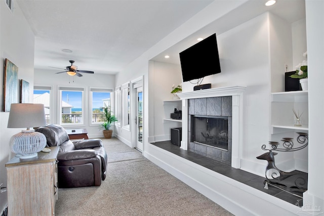 carpeted living room with ceiling fan and a tiled fireplace