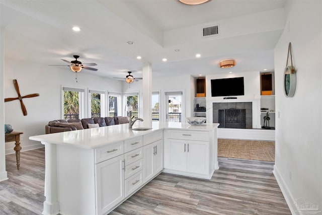 kitchen featuring kitchen peninsula, light wood-type flooring, sink, a tile fireplace, and white cabinets