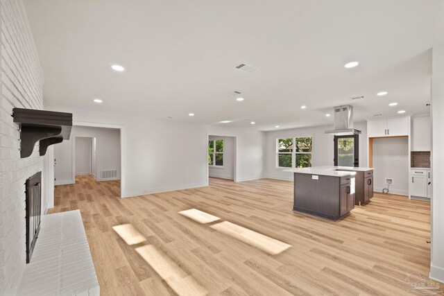 unfurnished living room featuring light wood finished floors, a brick fireplace, visible vents, and baseboards