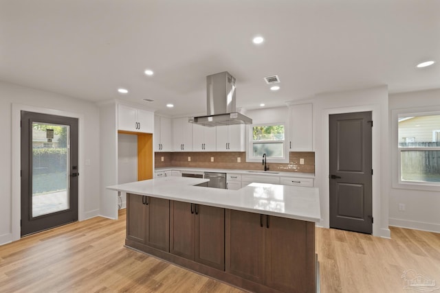 kitchen featuring light countertops, visible vents, island range hood, stainless steel dishwasher, and a sink