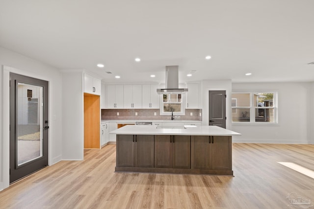 kitchen with a center island, island exhaust hood, light wood finished floors, light countertops, and white cabinets