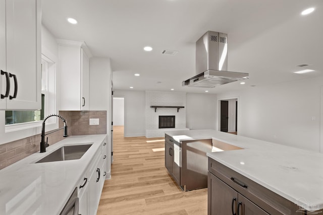 kitchen featuring light wood finished floors, a sink, open floor plan, white cabinetry, and island range hood
