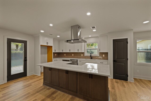 kitchen featuring a sink, island exhaust hood, light countertops, white cabinets, and visible vents