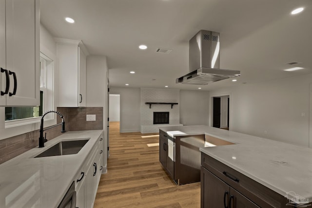 kitchen with island exhaust hood, light wood finished floors, a sink, open floor plan, and white cabinetry