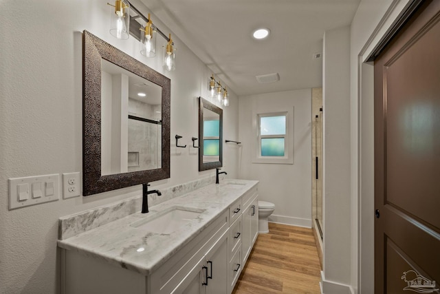 bathroom featuring a shower stall, double vanity, wood finished floors, toilet, and a sink