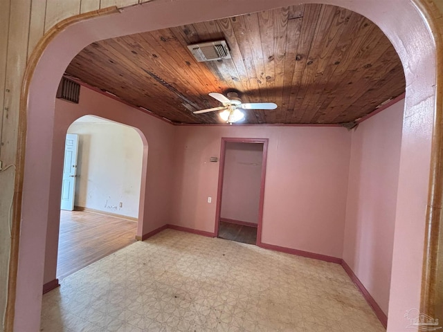 empty room featuring light floors, wood ceiling, arched walkways, and baseboards