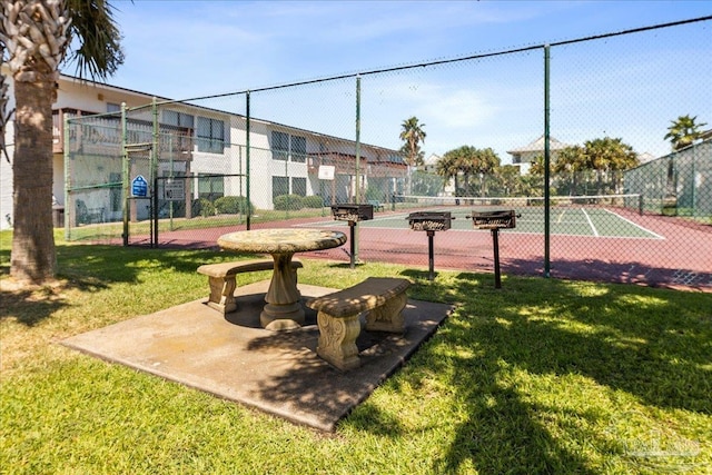 view of property's community featuring a tennis court, fence, and a lawn