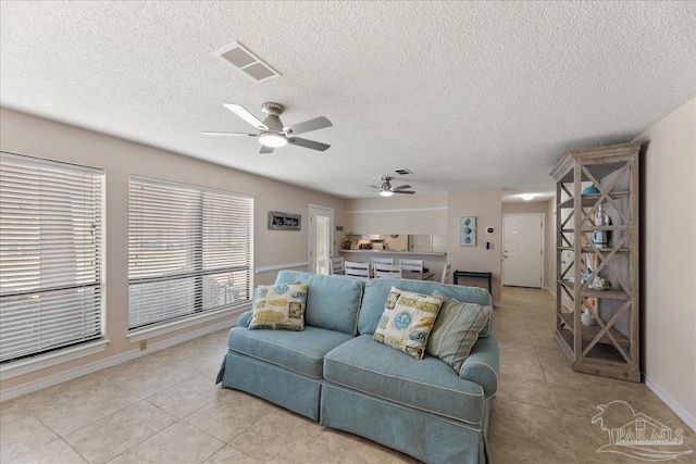 living area with a textured ceiling, light tile patterned flooring, visible vents, and baseboards