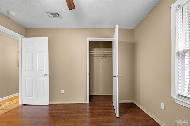 unfurnished bedroom featuring ceiling fan, a textured ceiling, a closet, and dark hardwood / wood-style floors