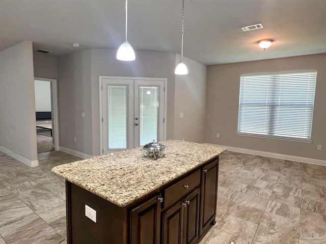 kitchen with hanging light fixtures, light stone counters, a kitchen island, dark brown cabinets, and french doors