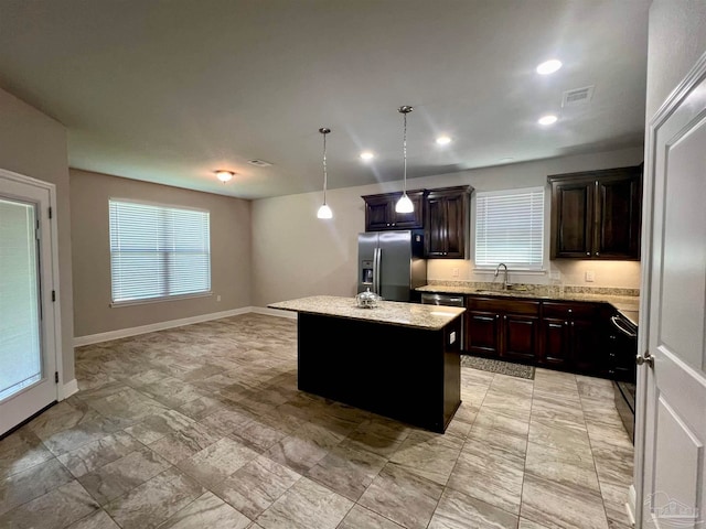 kitchen featuring light stone counters, dark brown cabinetry, stainless steel fridge, decorative light fixtures, and a center island