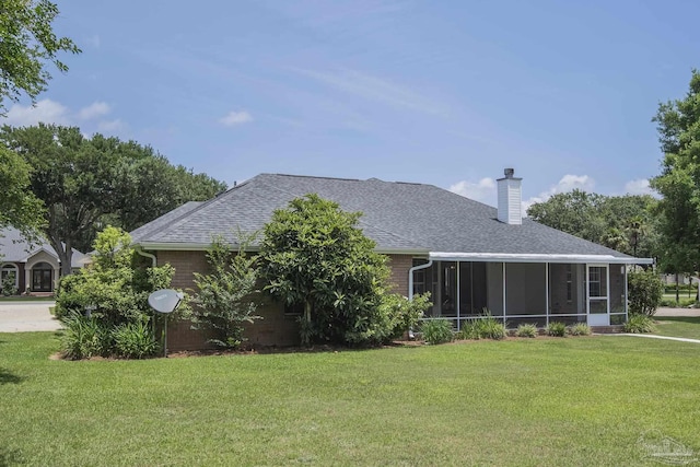 3221 Cobblestone Dr, Pace, FL 32571 - rear view of house with a lawn, a chimney, a sunroom, a shingled roof, and brick siding