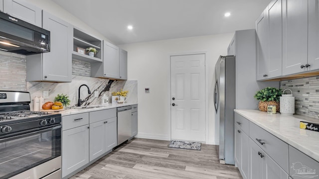 kitchen featuring stainless steel appliances, sink, light wood-type flooring, light stone counters, and tasteful backsplash