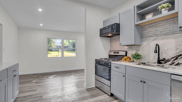 kitchen featuring light stone counters, backsplash, appliances with stainless steel finishes, light hardwood / wood-style floors, and sink