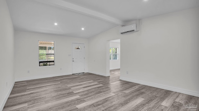 unfurnished room featuring a wall unit AC, lofted ceiling with beams, and light wood-type flooring