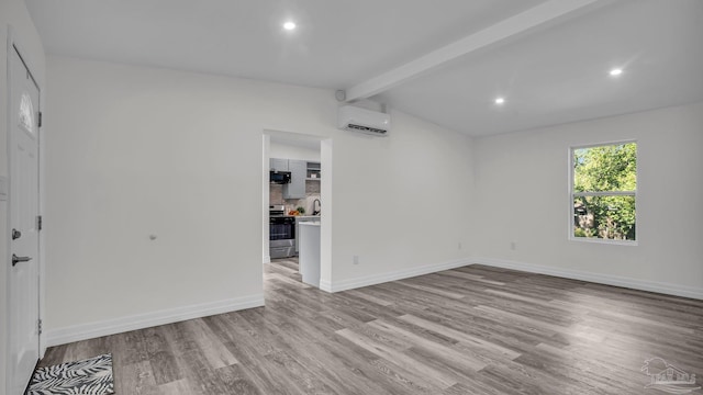 unfurnished room with an AC wall unit, light hardwood / wood-style flooring, and lofted ceiling with beams