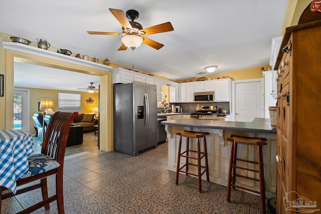 kitchen featuring dark countertops, a peninsula, appliances with stainless steel finishes, and white cabinets