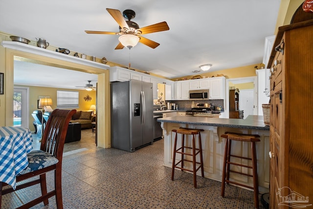 kitchen featuring dark countertops, appliances with stainless steel finishes, a breakfast bar, a peninsula, and white cabinetry