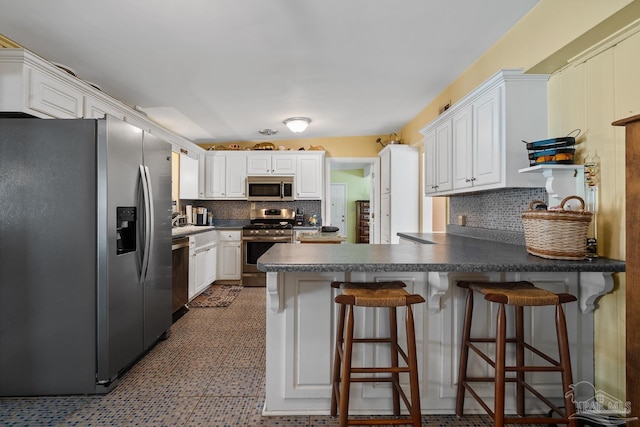 kitchen with appliances with stainless steel finishes, dark countertops, white cabinets, and a peninsula