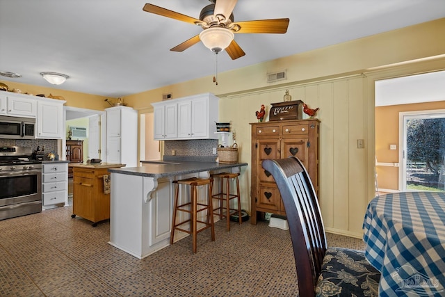 kitchen featuring visible vents, dark countertops, appliances with stainless steel finishes, a peninsula, and white cabinetry