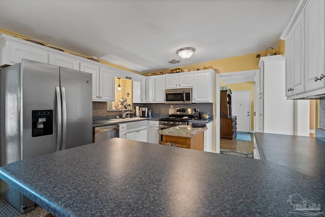 kitchen with stainless steel appliances, dark countertops, backsplash, and white cabinets