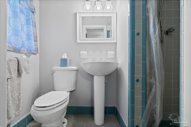 bathroom with toilet, tile patterned flooring, baseboards, and a tile shower