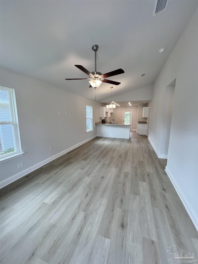 unfurnished living room with lofted ceiling, ceiling fan with notable chandelier, and light wood-type flooring