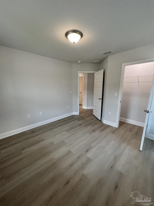 unfurnished bedroom featuring hardwood / wood-style flooring, a closet, a spacious closet, and a textured ceiling