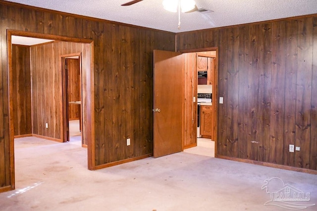 carpeted empty room with ceiling fan, wooden walls, and a textured ceiling