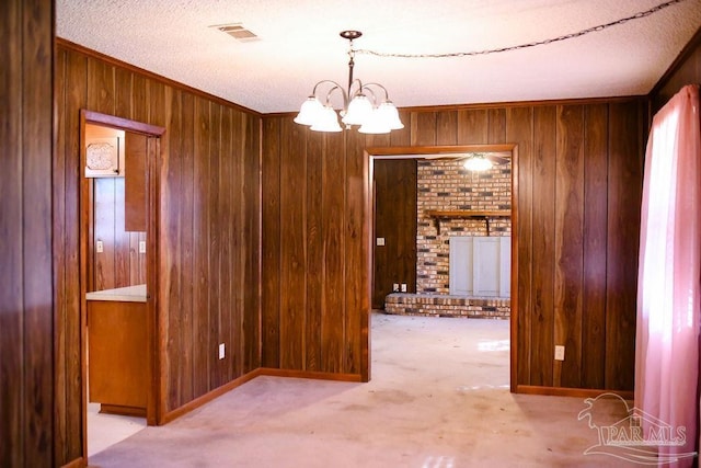 carpeted empty room with a textured ceiling, wooden walls, and a notable chandelier