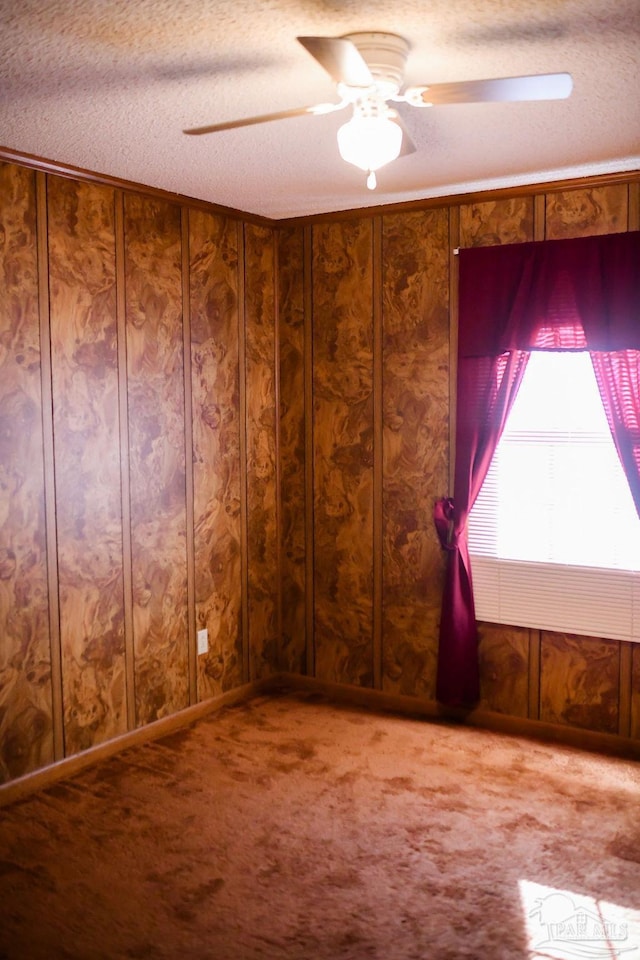 unfurnished room with carpet, a textured ceiling, ceiling fan, and wood walls