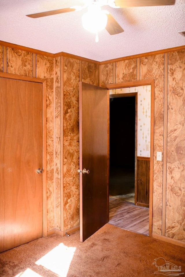 carpeted spare room featuring ceiling fan, crown molding, a textured ceiling, and wooden walls