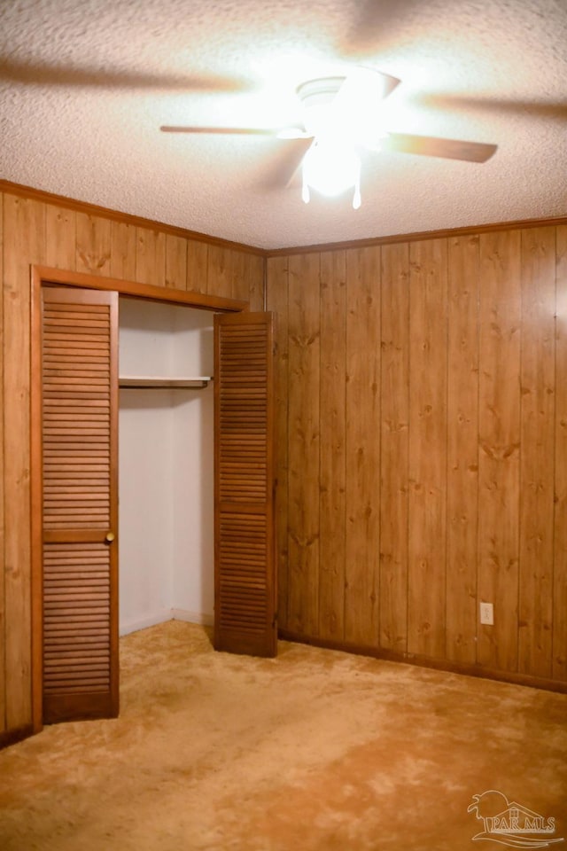 unfurnished bedroom with wooden walls, ceiling fan, a textured ceiling, carpet floors, and a closet