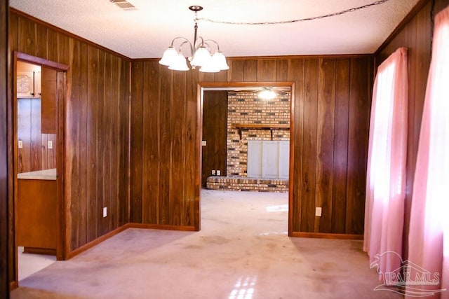 carpeted empty room with wooden walls, a textured ceiling, and an inviting chandelier