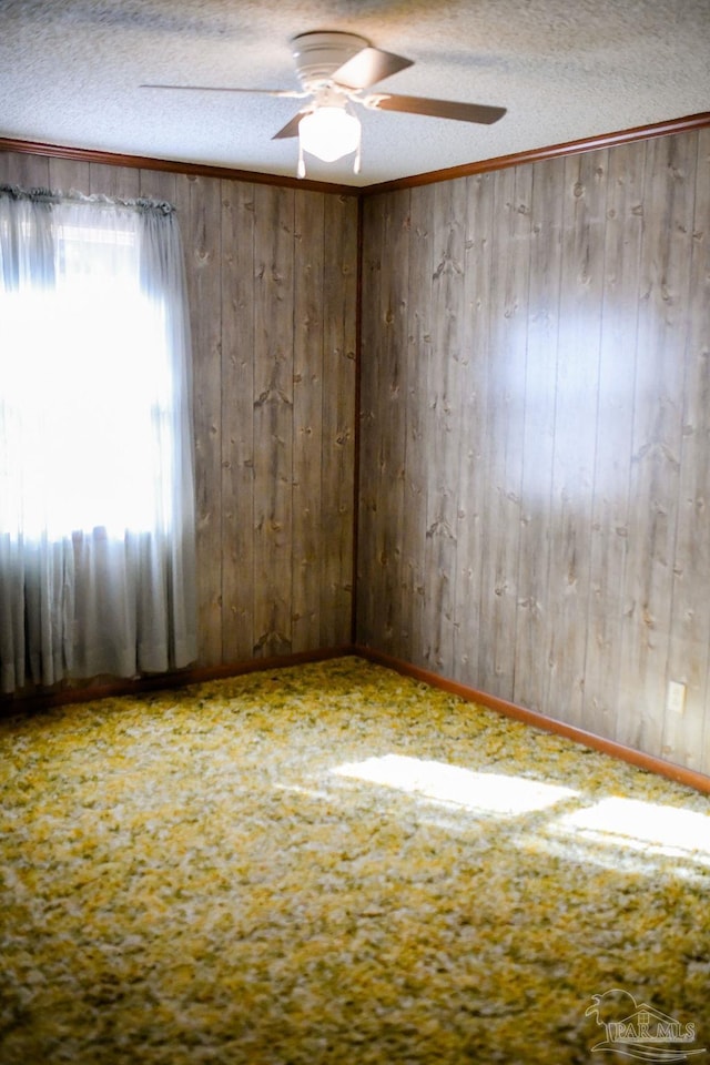 carpeted spare room featuring a textured ceiling, ceiling fan, and wood walls