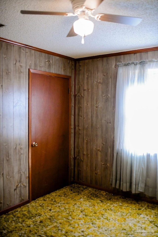 unfurnished room featuring ceiling fan, wooden walls, a textured ceiling, and ornamental molding