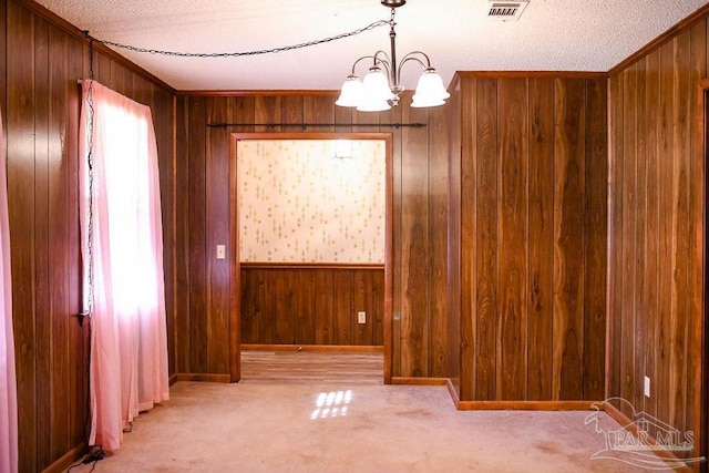 unfurnished room with wooden walls, a textured ceiling, and an inviting chandelier